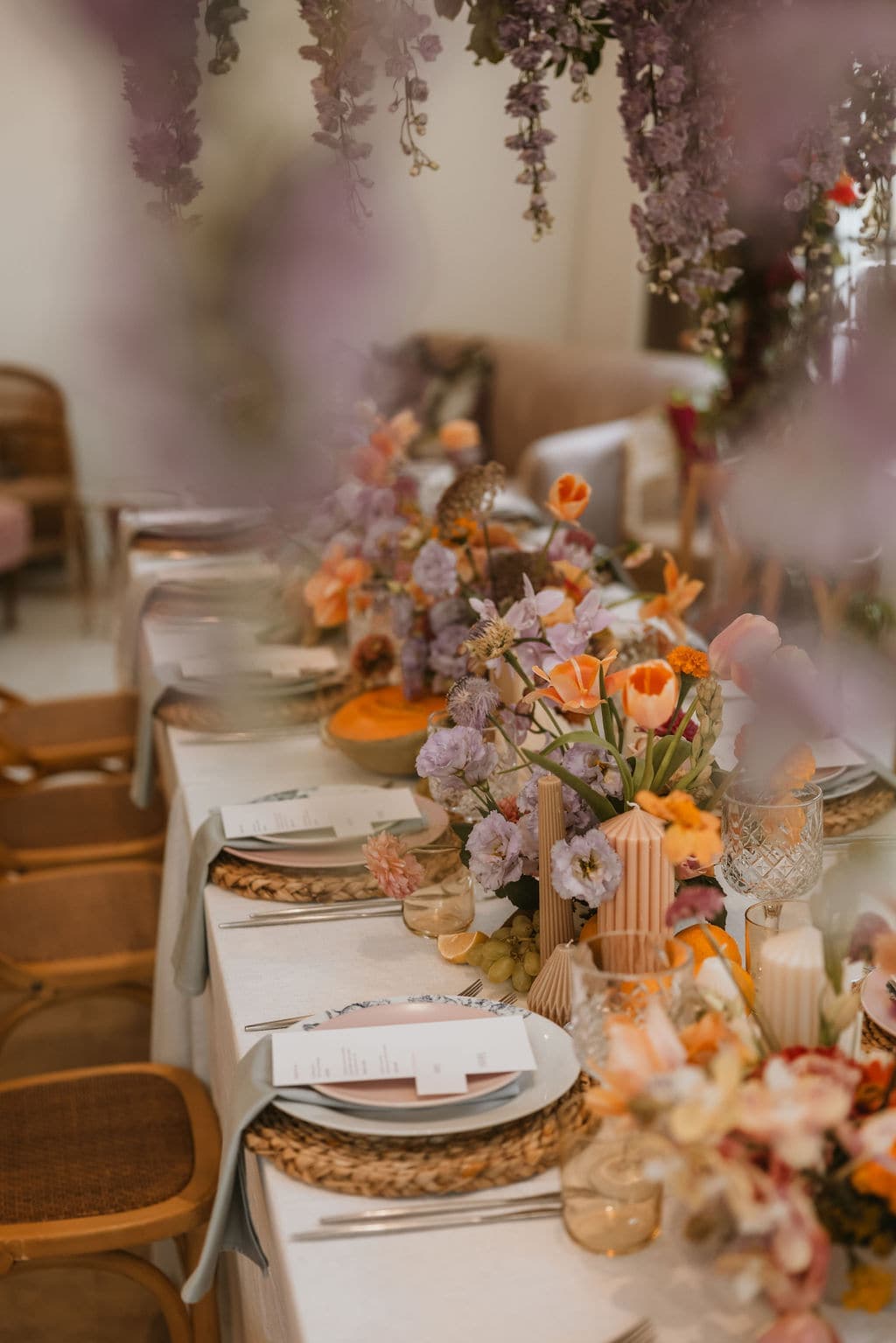 A long tablescape dressed with orange and lilac flowers