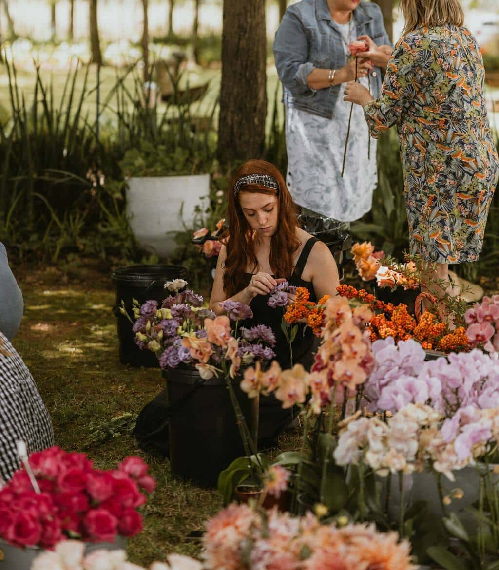 Florists working from buckets of lisianthus, orchids and garden roses in dappled light