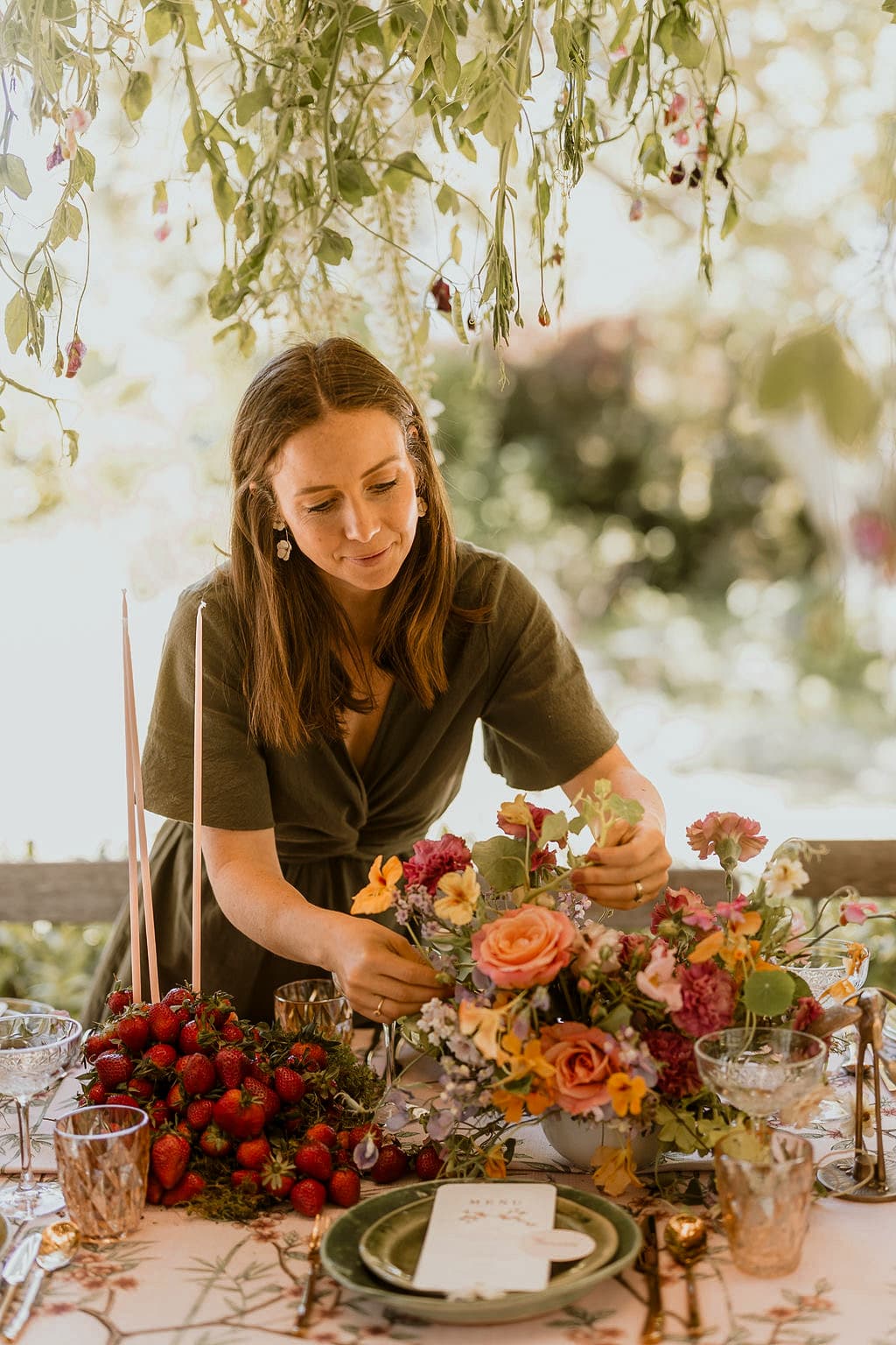 Pippa arranging a colorful centerpiece of garden roses and strawberries at an outdoor table